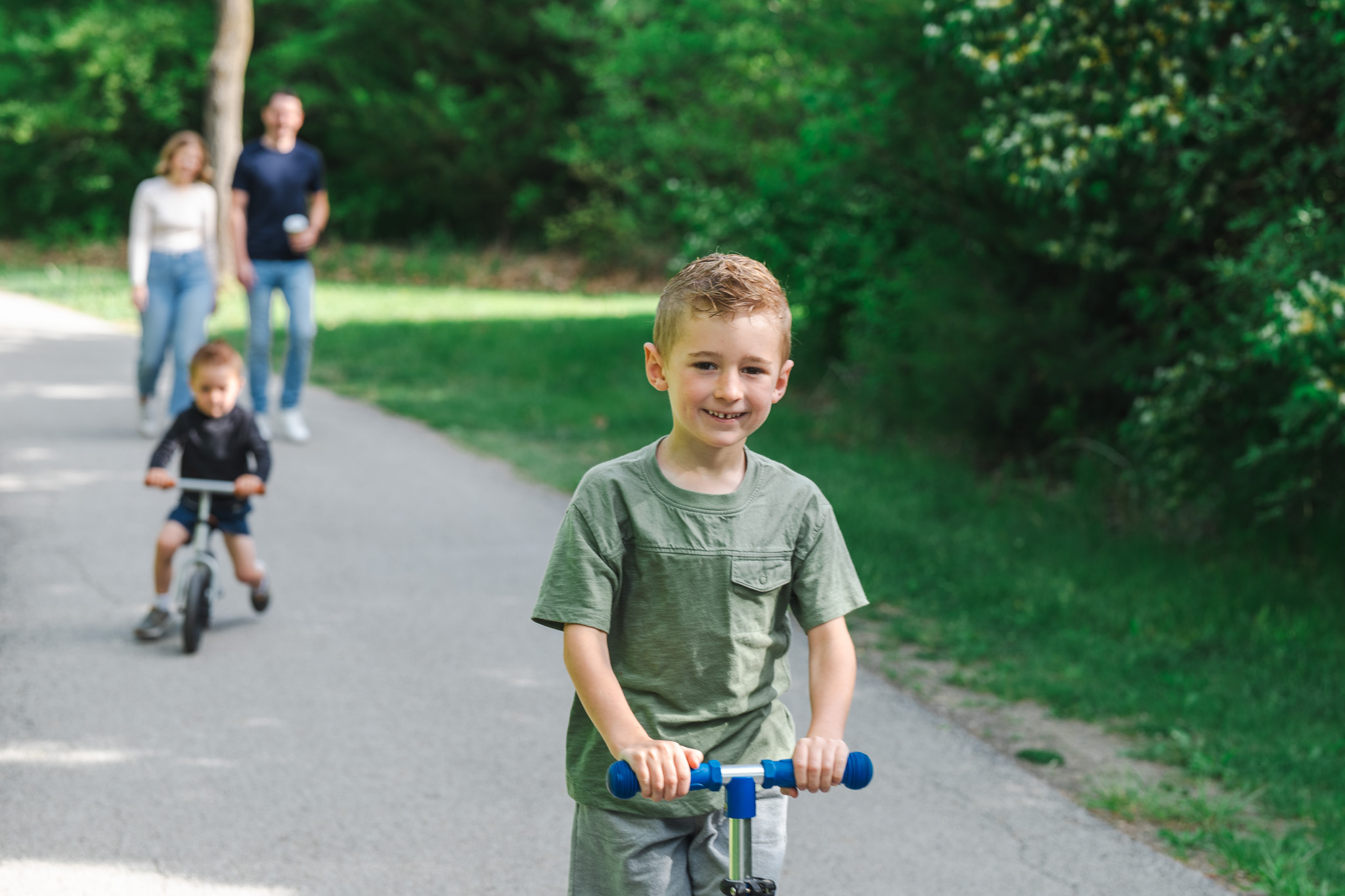 Omaha family lifestyle session — kids on scooter and balance bike along a park path